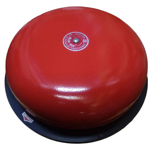 A red fire alarm bell with a black base, featuring a central white and red label and a small sticker on the lower left, set against a plain white background.