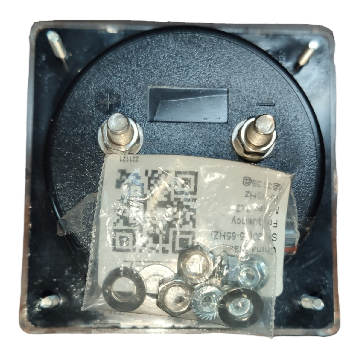 A square black electrical component or switch with two metal terminal screws and a small rectangular slot, shown with a clear plastic bag containing washers and nuts attached in front. A QR code and printed text are visible on the tag.
