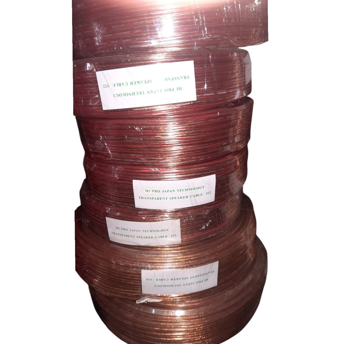 A stack of copper-colored speaker wire spools wrapped in clear plastic, with white labels showing text including 'III PRO JAPAN TECHNOLOGIES' and 'TRANSMITTER SPEAKER CABLE'.