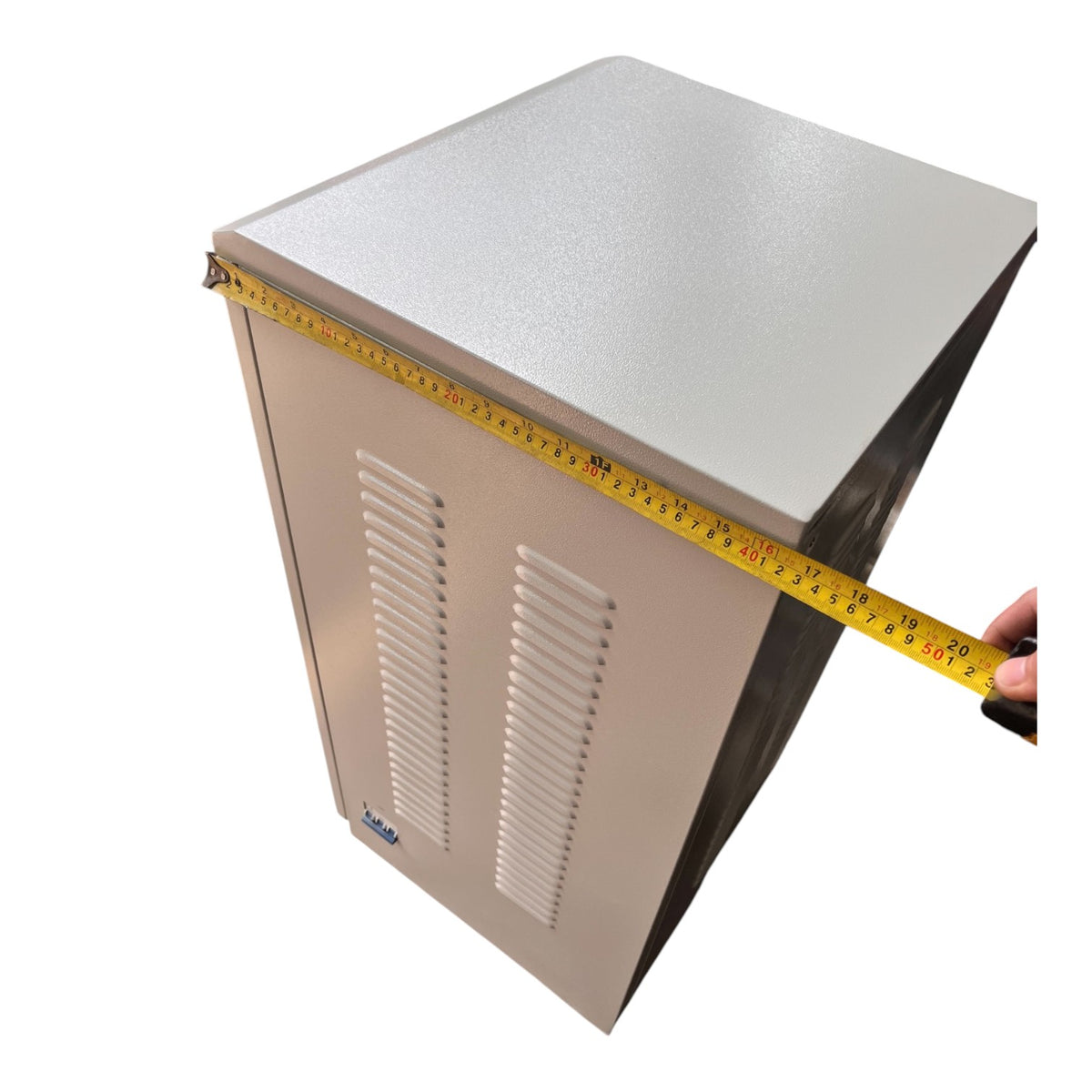 A beige metal equipment cabinet with a yellow tape measure stretched across it to show dimensions, held by a hand on the right side, against a plain white background.