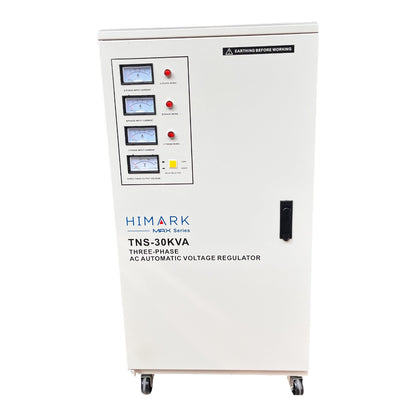 A white HIMARK TNS-30KVA three-phase AC automatic voltage regulator cabinet on wheels, featuring a front panel with multiple analog meters, red emergency stop buttons, and a black warning label.