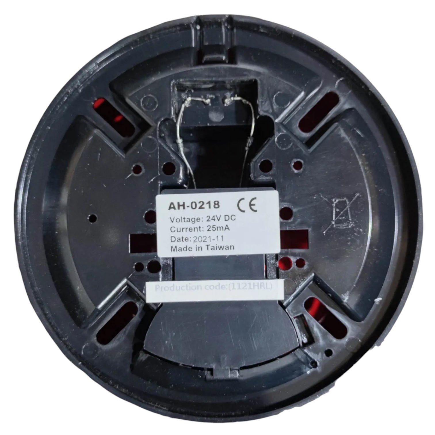 The underside of a round black plastic electrical component, likely a thermostat or similar home automation device, featuring a white label with technical specifications and red internal contacts.