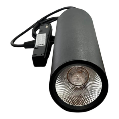 A black cylindrical track spotlight with a textured metallic silver reflector and a black power adapter with attached cable, shown on a plain white background.