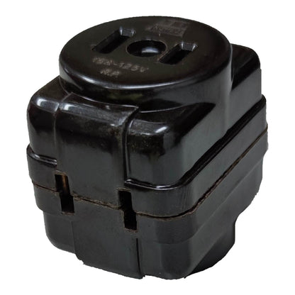 A black plastic electrical outlet adapter or junction block with a circular top featuring a two-prong outlet cutout, photographed on a plain white background.