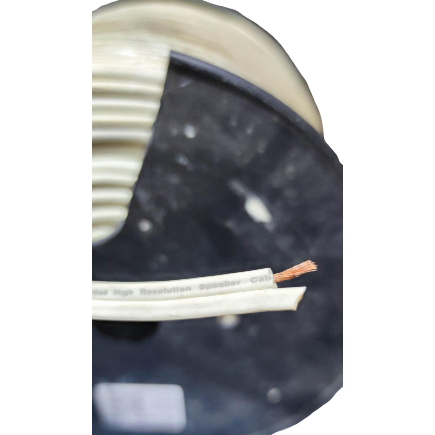 A close-up of a spool of white speaker wire, with one strand cut open to show the copper wire core, set against a dark background.