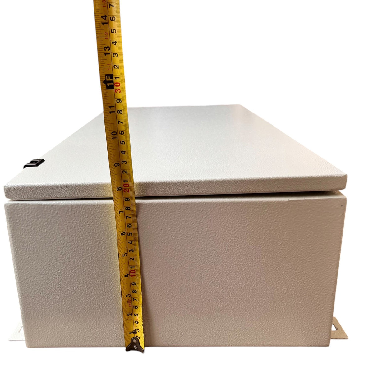 A light beige textured metal electrical junction box shown with a yellow tape measure standing vertically to indicate its height against a plain white background.