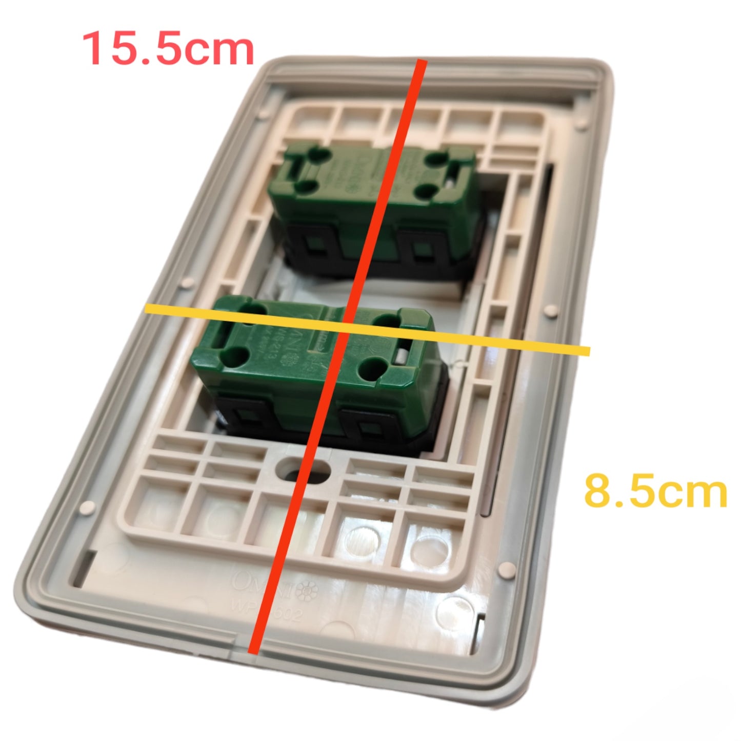 A two-gang wall switch plate backplate with two green terminal blocks, overlaid with red and yellow measurement lines and text indicating dimensions 15.5cm and 8.