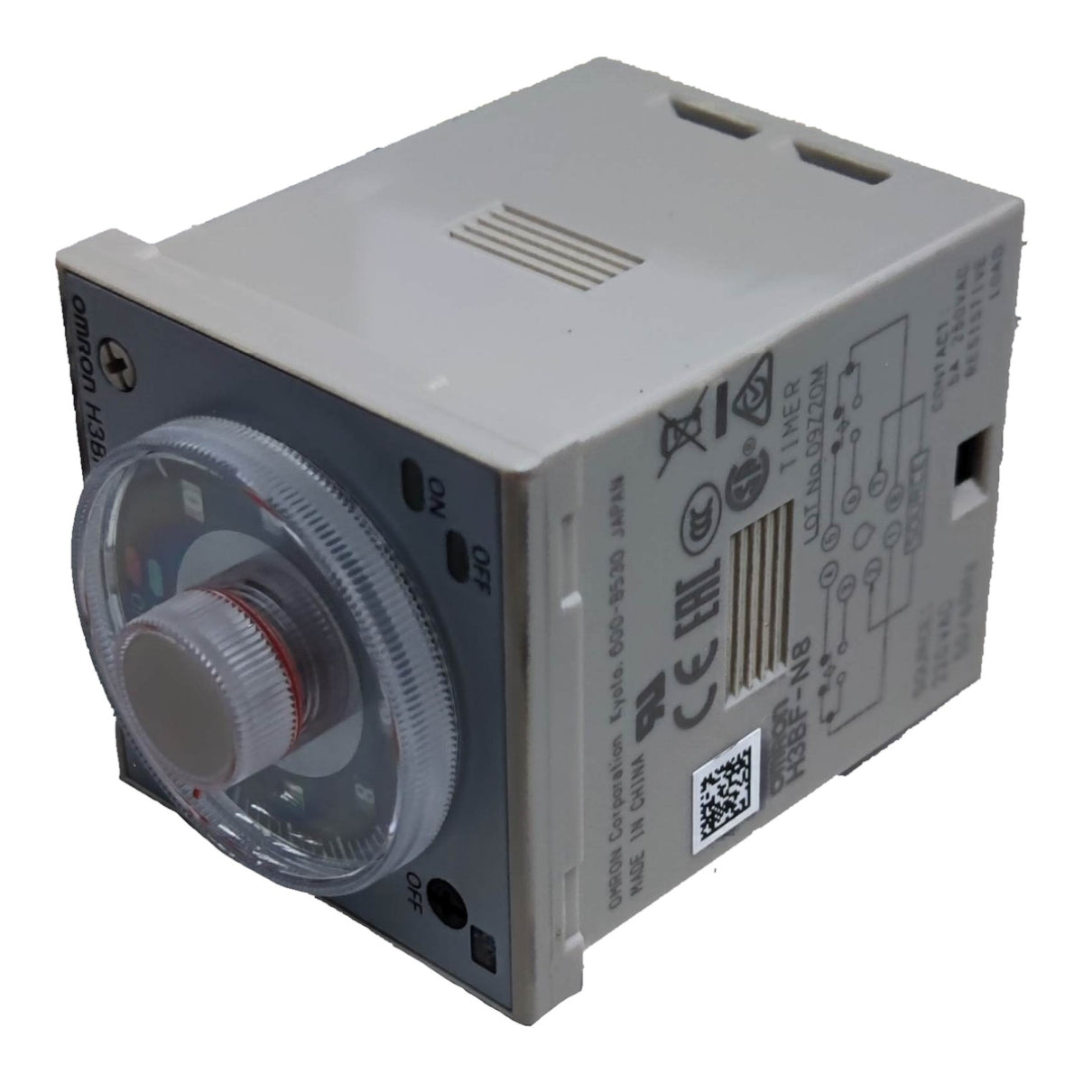 A compact electrical timer relay module with a gray plastic housing, a front dial window, and printed technical specifications and wiring diagrams on the side.