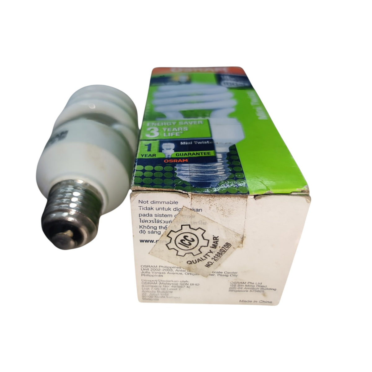 A CFL compact fluorescent light bulb with a silver E10 base shown next to its original green and white packaging box on a white background.