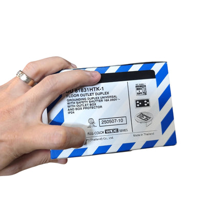 A hand holding a blue and white striped box of THOR Floor Outlet Duplex GFCI Outlet Universal, with product text and icons visible on the side.