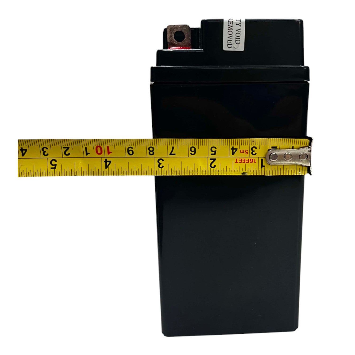 A black rectangular battery with a yellow tape measure stretched horizontally across it to show its width, photographed on a plain white background.