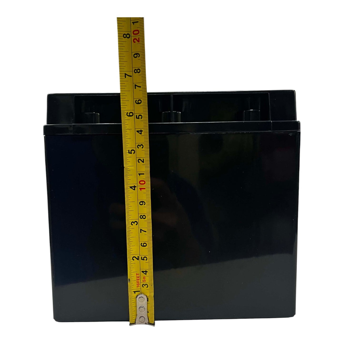 A black rectangular battery with a yellow tape measure standing vertically against it to show its height, photographed on a plain white background.