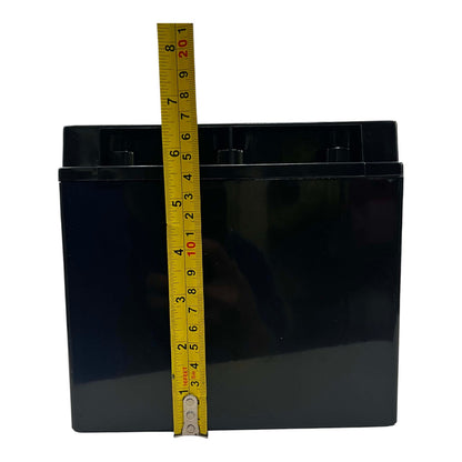 A black rectangular battery with a yellow tape measure standing vertically against it to show its height, photographed on a plain white background.