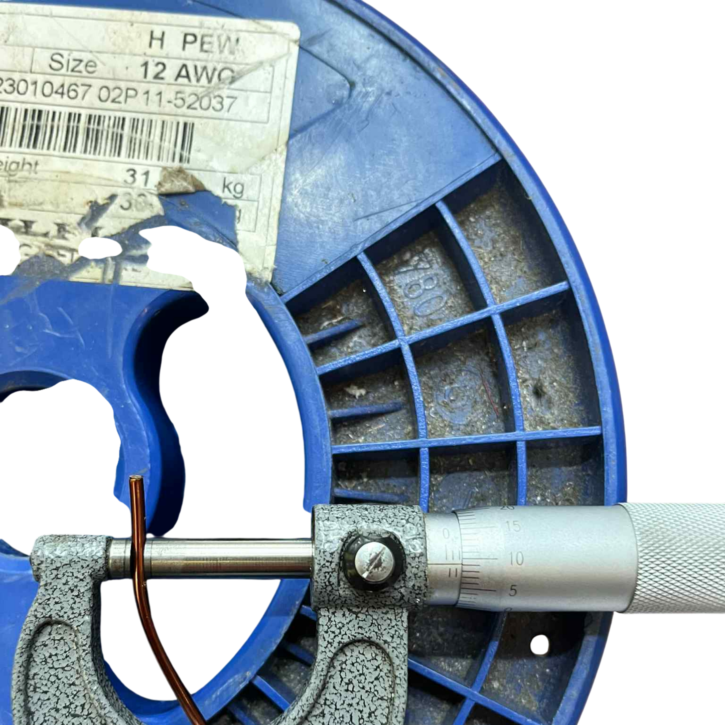 Close-up of a blue micrometer measuring a spool of wire.