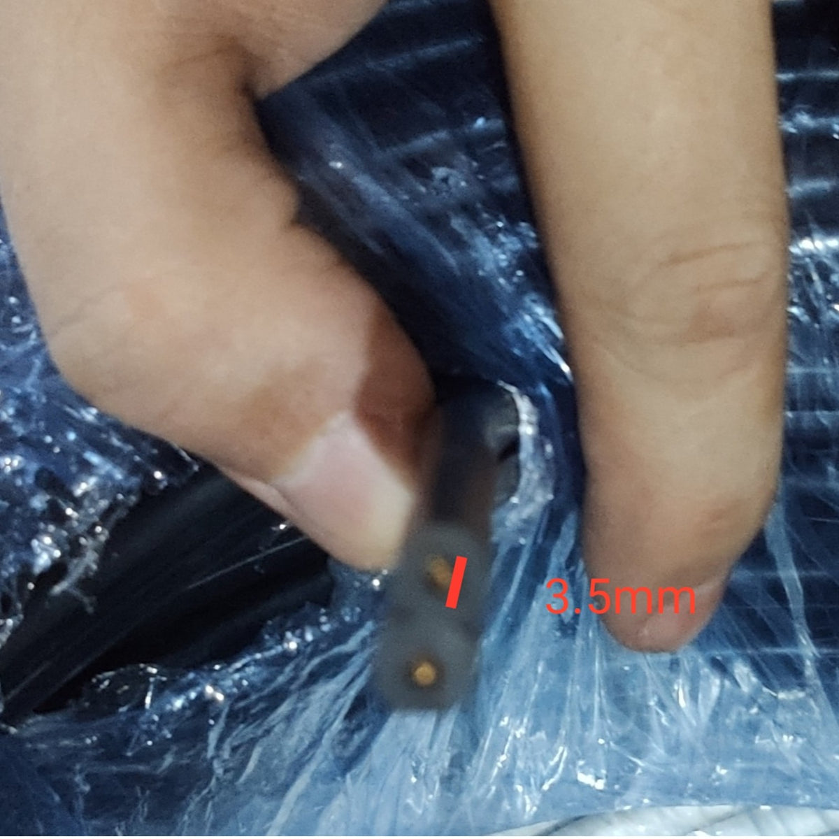 A close-up of a hand holding a black cable with a cross-section labeled '3.5mm' on a crinkled clear plastic surface.