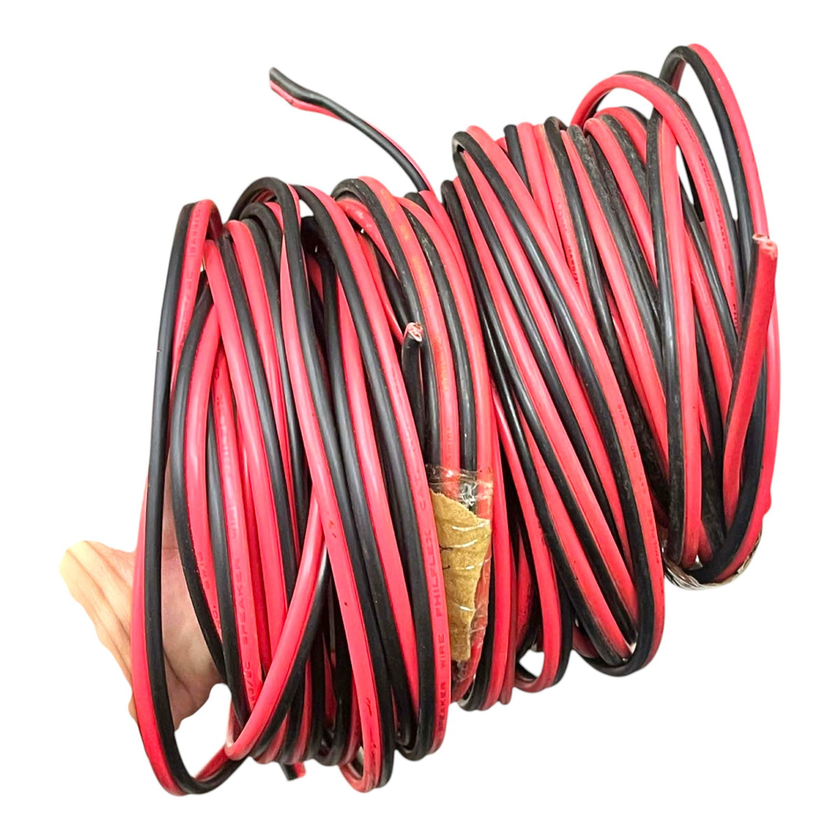 A coiled bundle of red and black electrical wire or cable, held together by a hand at the left edge, isolated on a white background.