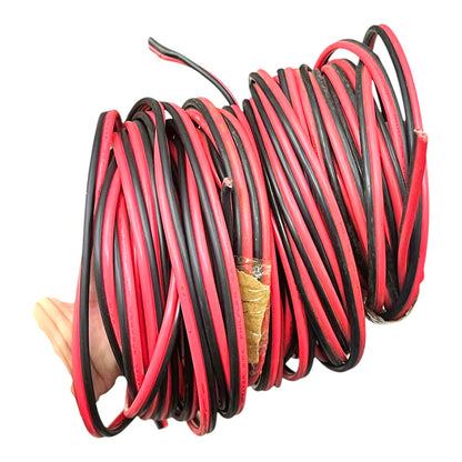 A coiled bundle of red and black electrical wire or cable, held together by a hand at the left edge, isolated on a white background.