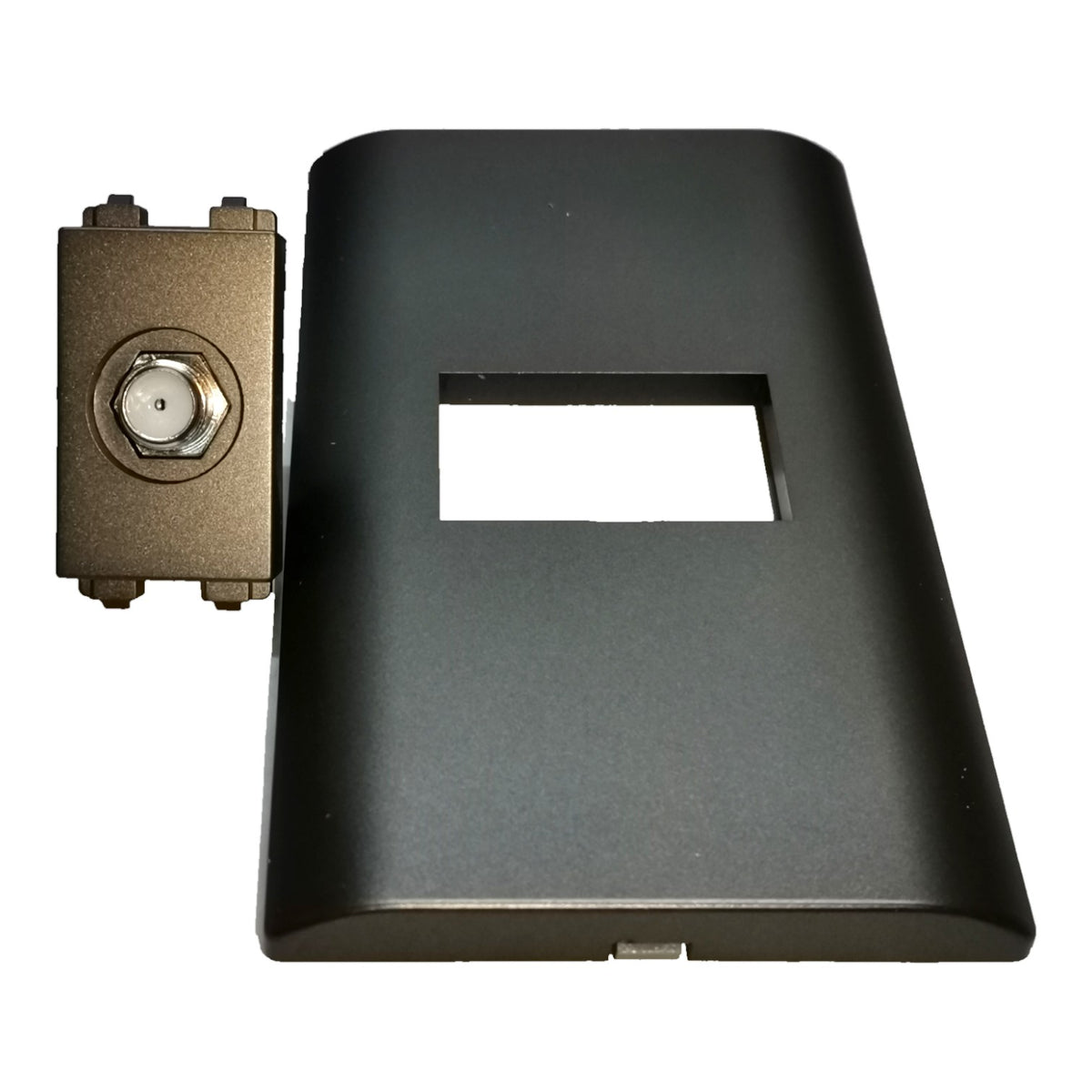 A black plastic rectangular cover with a central rectangular cutout, shown next to a small bronze metal connector component on a plain white background.