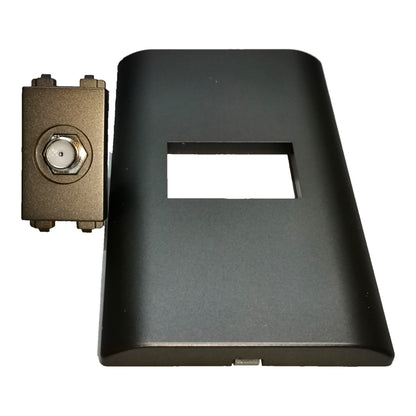 A black plastic rectangular cover with a central rectangular cutout, shown next to a small bronze metal connector component on a plain white background.
