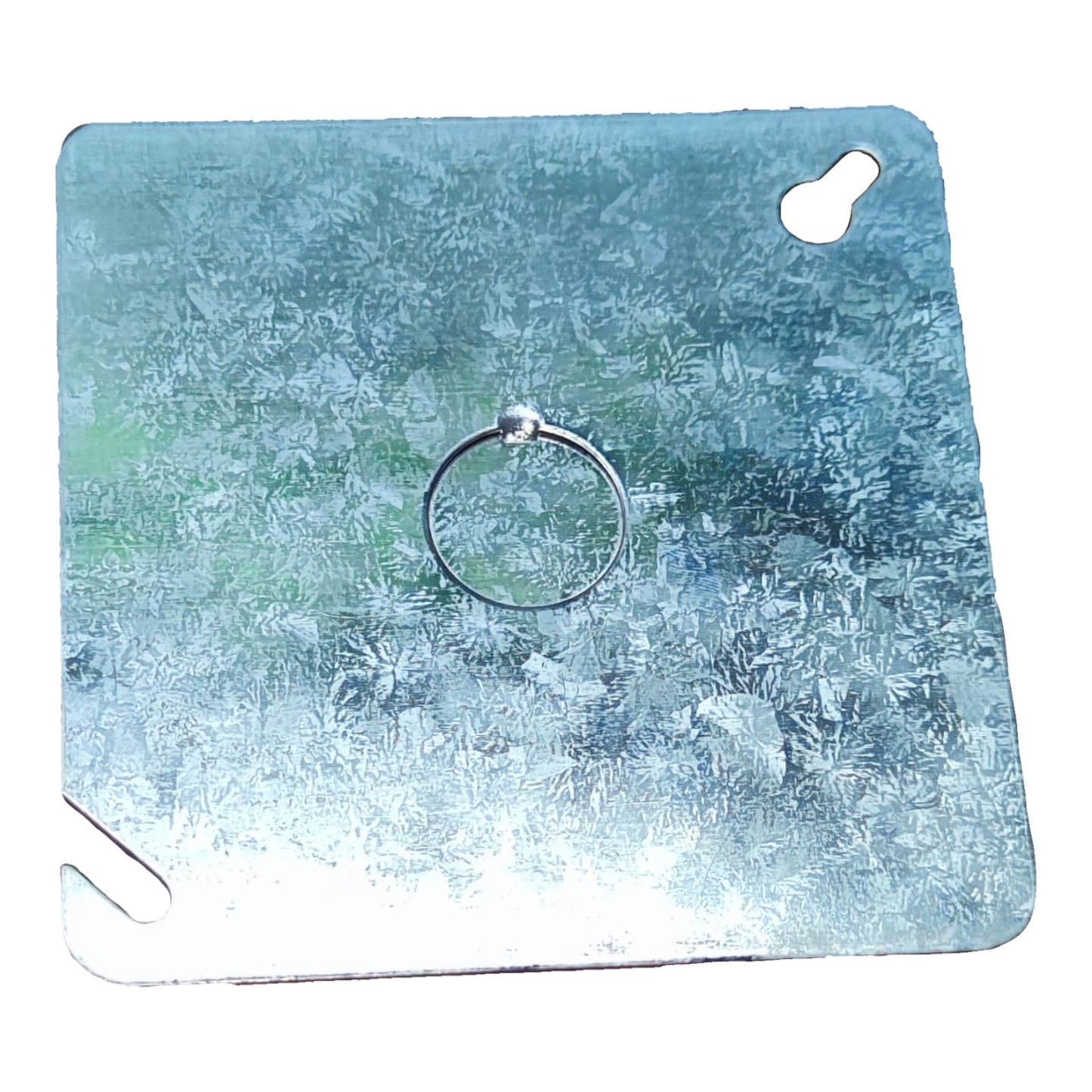 A silver metal ring with a small clear crystal or glass bead at the top, displayed on a square textured blue and green backing card with cutouts.