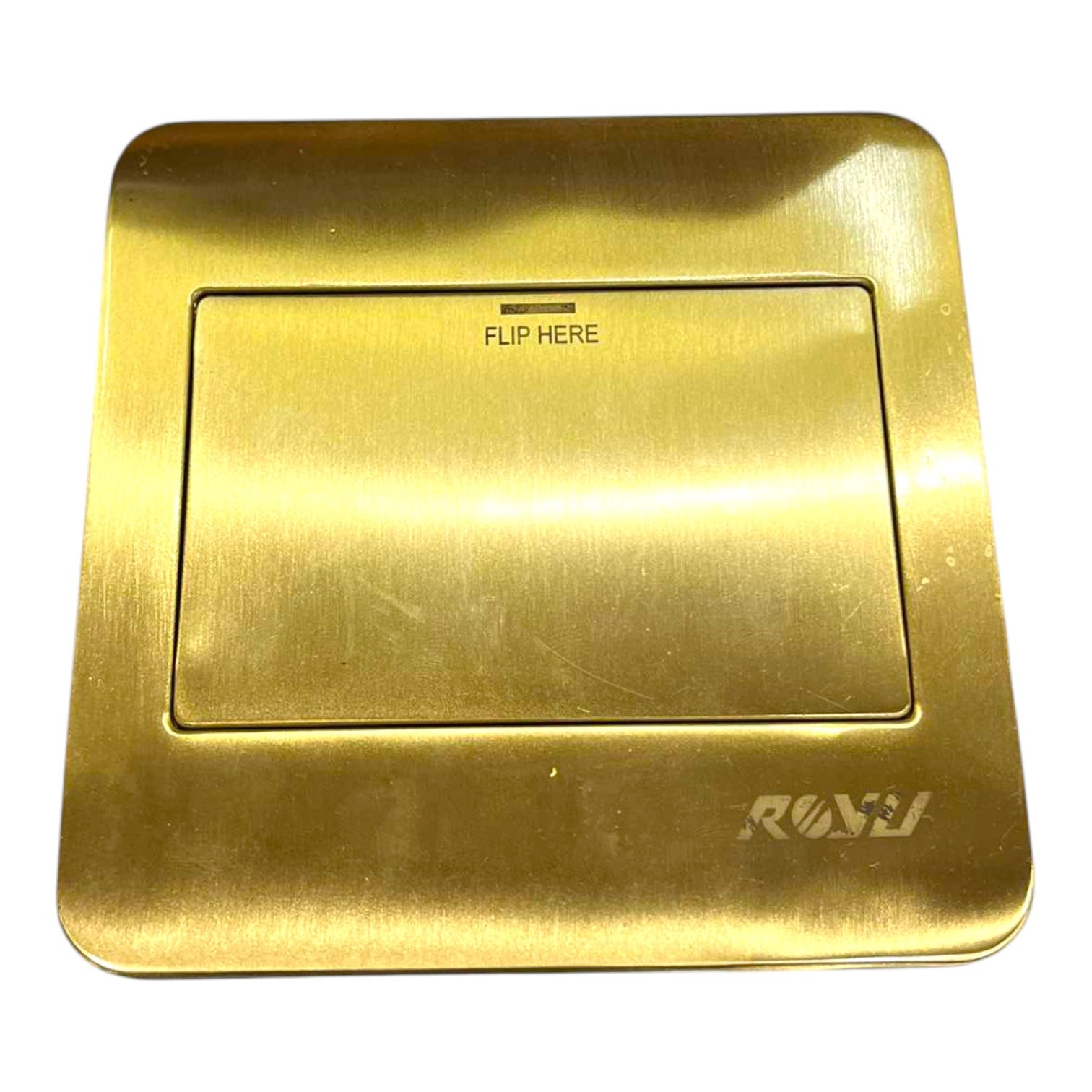 A brushed brass or gold-toned flush valve trim plate with a recessed center panel labeled 'FLIP HERE' and the brand name 'RAVI' in the bottom right corner, shown on a plain white background.