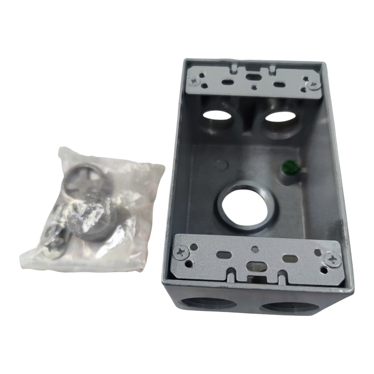 A gray metal electrical junction box with mounting hardware inside, shown next to a small clear plastic bag containing additional screws and washers on a white background.