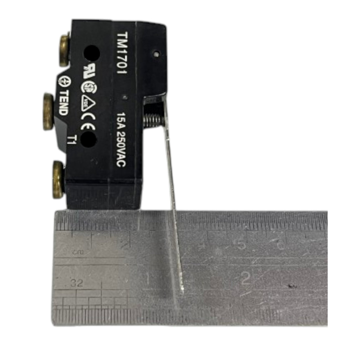 A small black electrical terminal block with brass screw terminals and white printed markings, shown next to a metal ruler for scale on a white background.