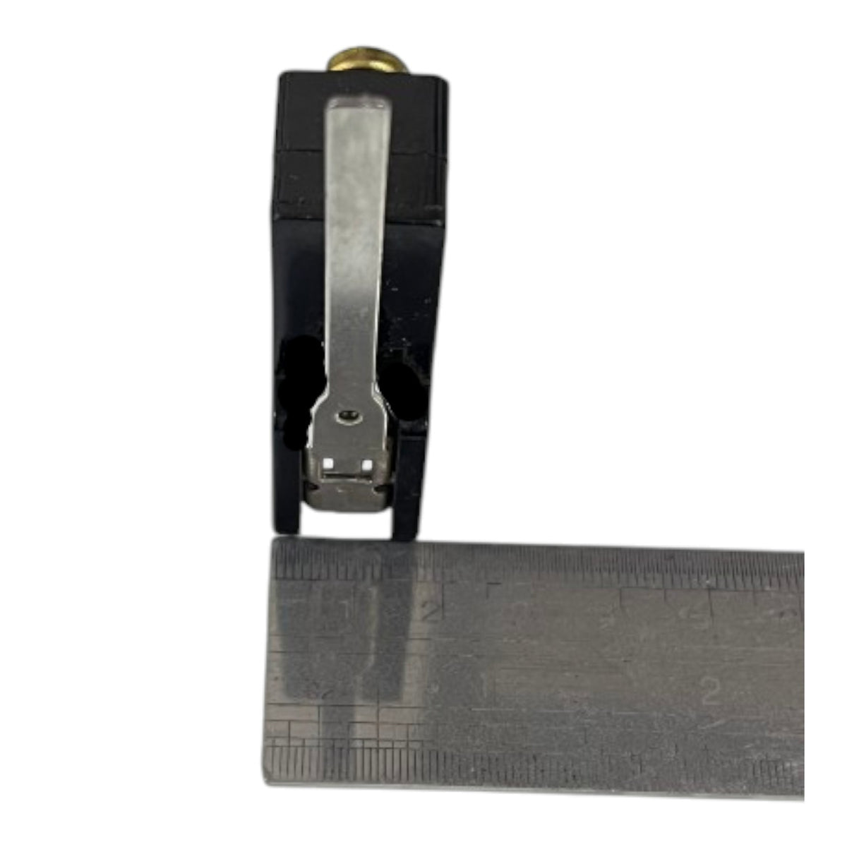 A black plastic and metal clamp-like tool with a ruler placed underneath it for scale, shown on a plain white background.