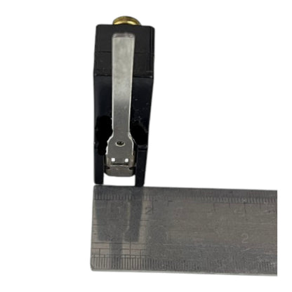 A black plastic and metal clamp-like tool with a ruler placed underneath it for scale, shown on a plain white background.