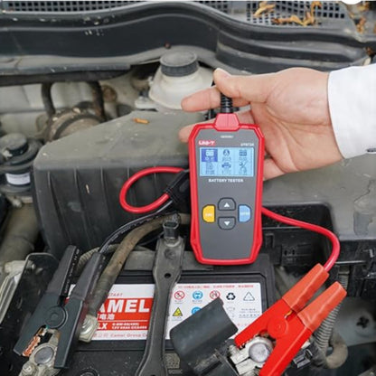 Person using a red battery tester on a car battery with a clear view of the engine compartment. UNI-T Digital Battery Tester 12V or 24V 250AH Max Capacity UT673A Electx Electrical Supply