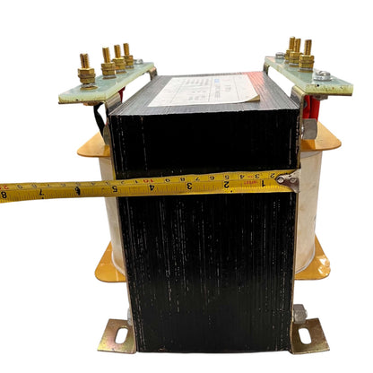 A large black and beige industrial transformer with brass-colored metal terminals and a yellow tape measure stretched horizontally across the front to show its width, isolated on a white background.