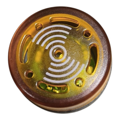 A round amber-brown and translucent gold plastic component with white concentric arc markings and several cutouts, shown on a plain white background.