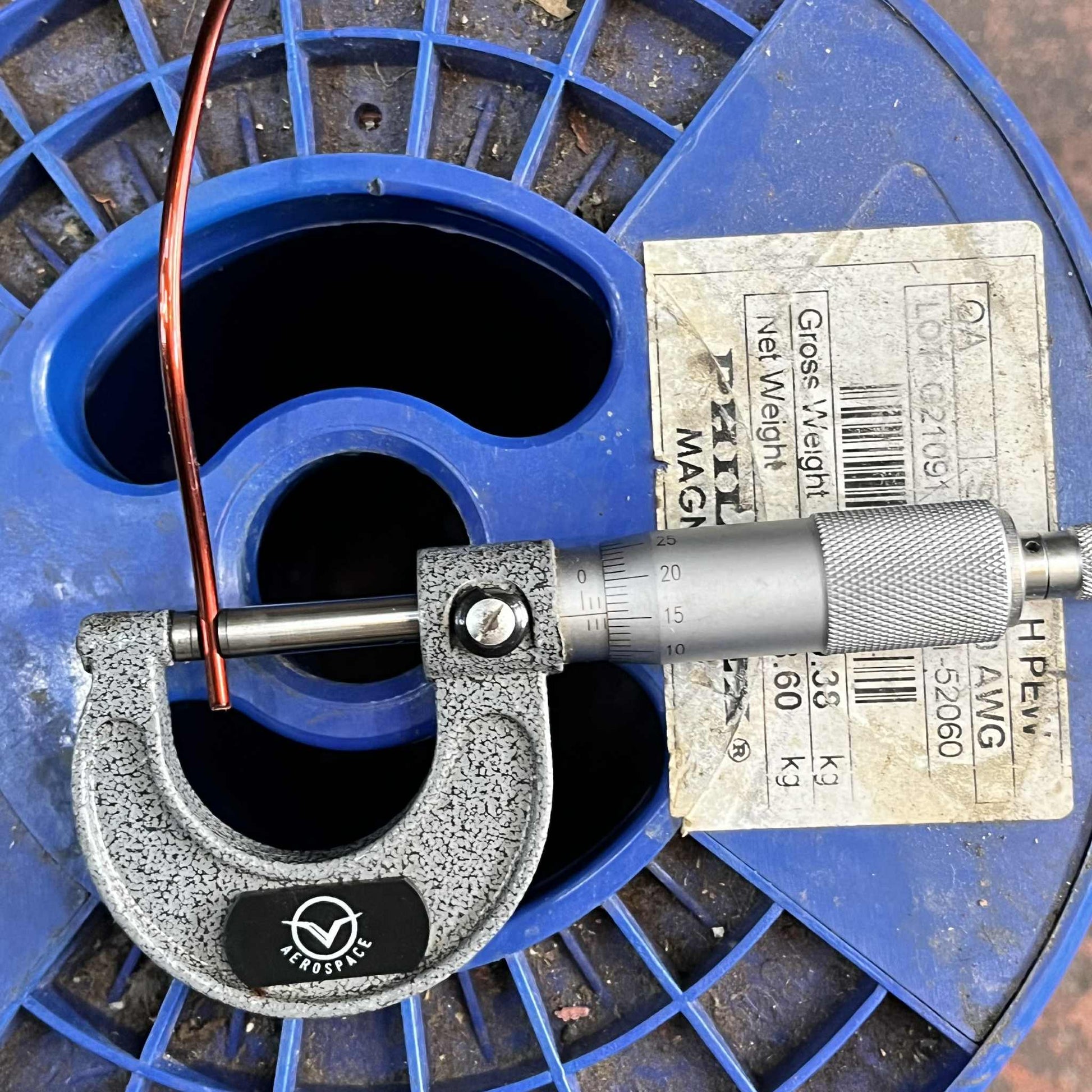 Measuring AWG 10 magnet wire for transformers on a blue spool using a micrometer