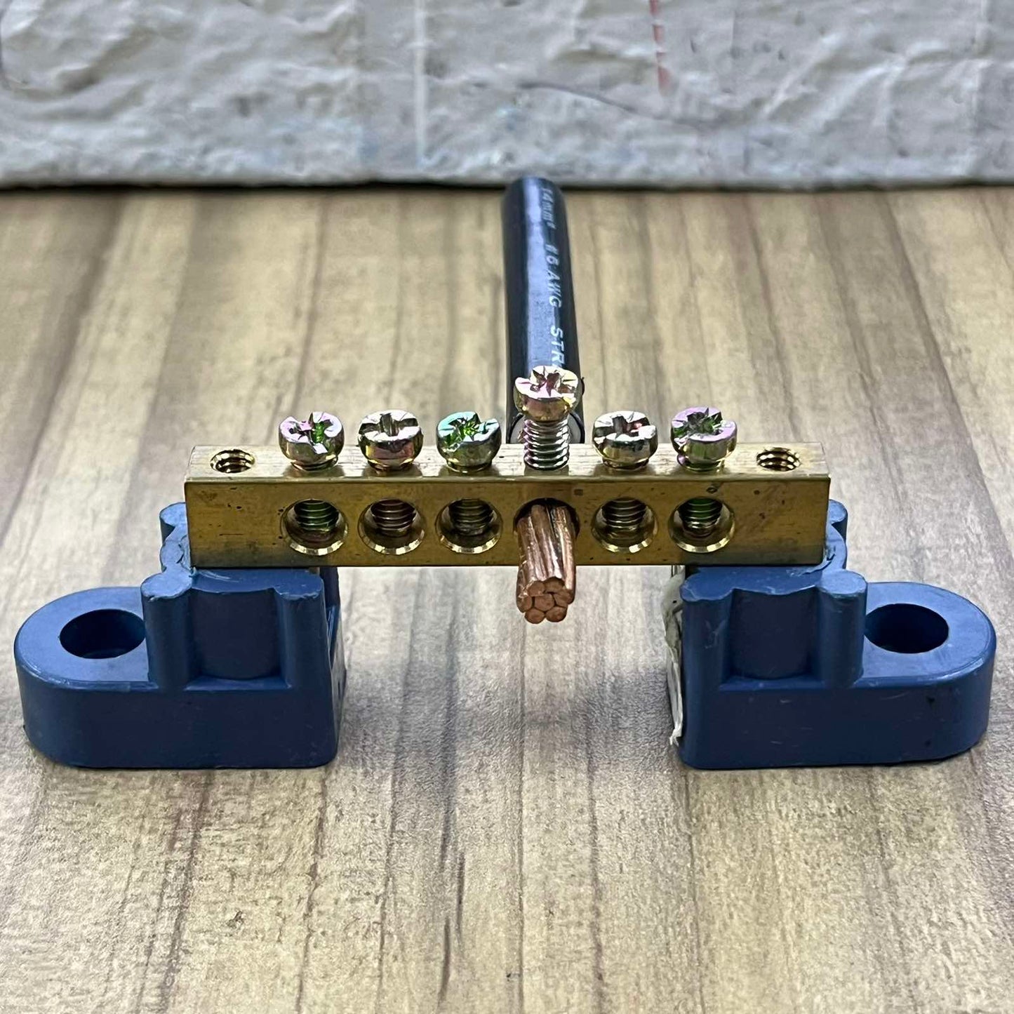 Grippes grounding bus bars 4 holes with mounted copper wire and blue mounting brackets on wooden surface