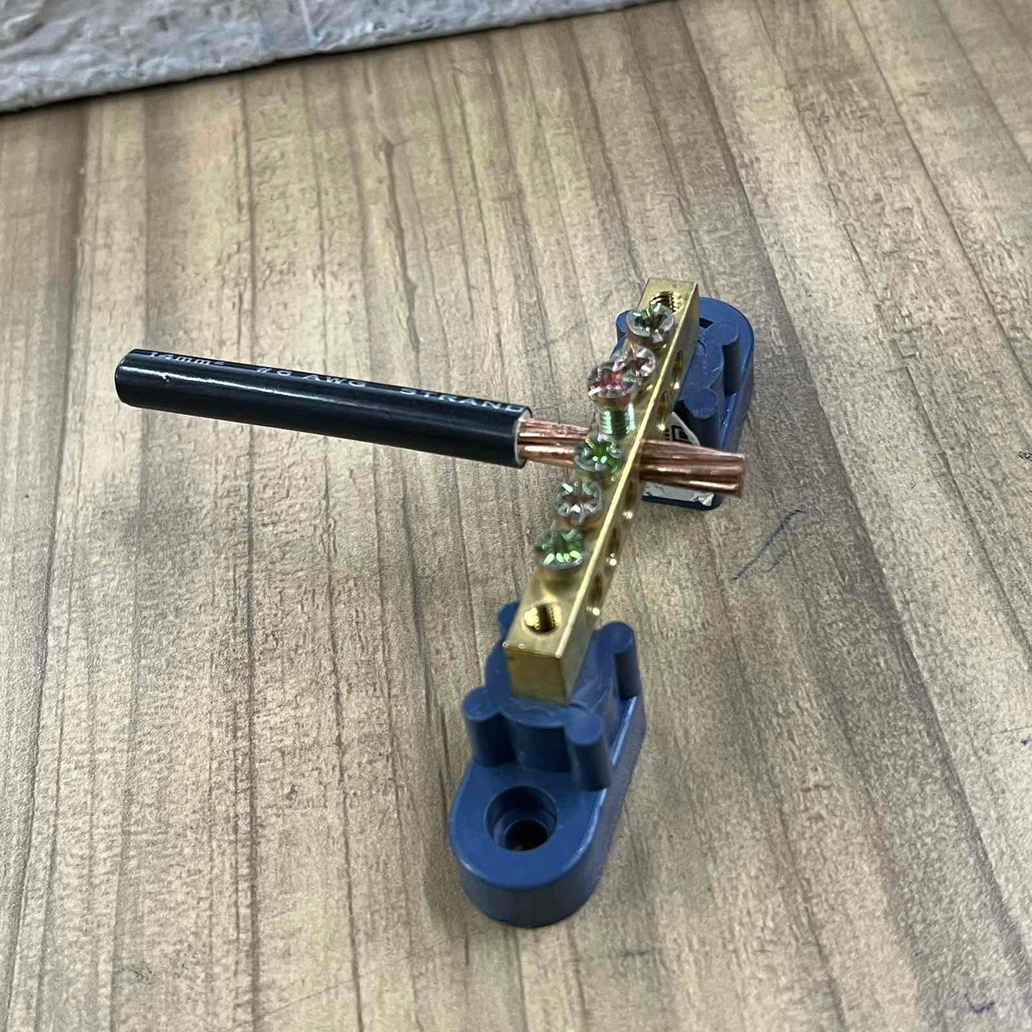 Grippes Electrical Grounding Bus Bars 4 Holes with attached copper wire on wooden surface