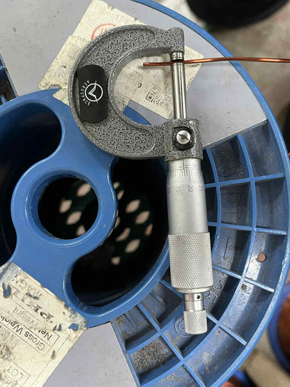 Measuring heavy duty magnet wire with a micrometer tool on a blue spool for precision assessment