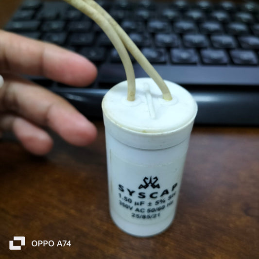 Close-up of a SYSCAP 1.5 microfarad capacitor with wires on a wooden surface and a keyboard in the background