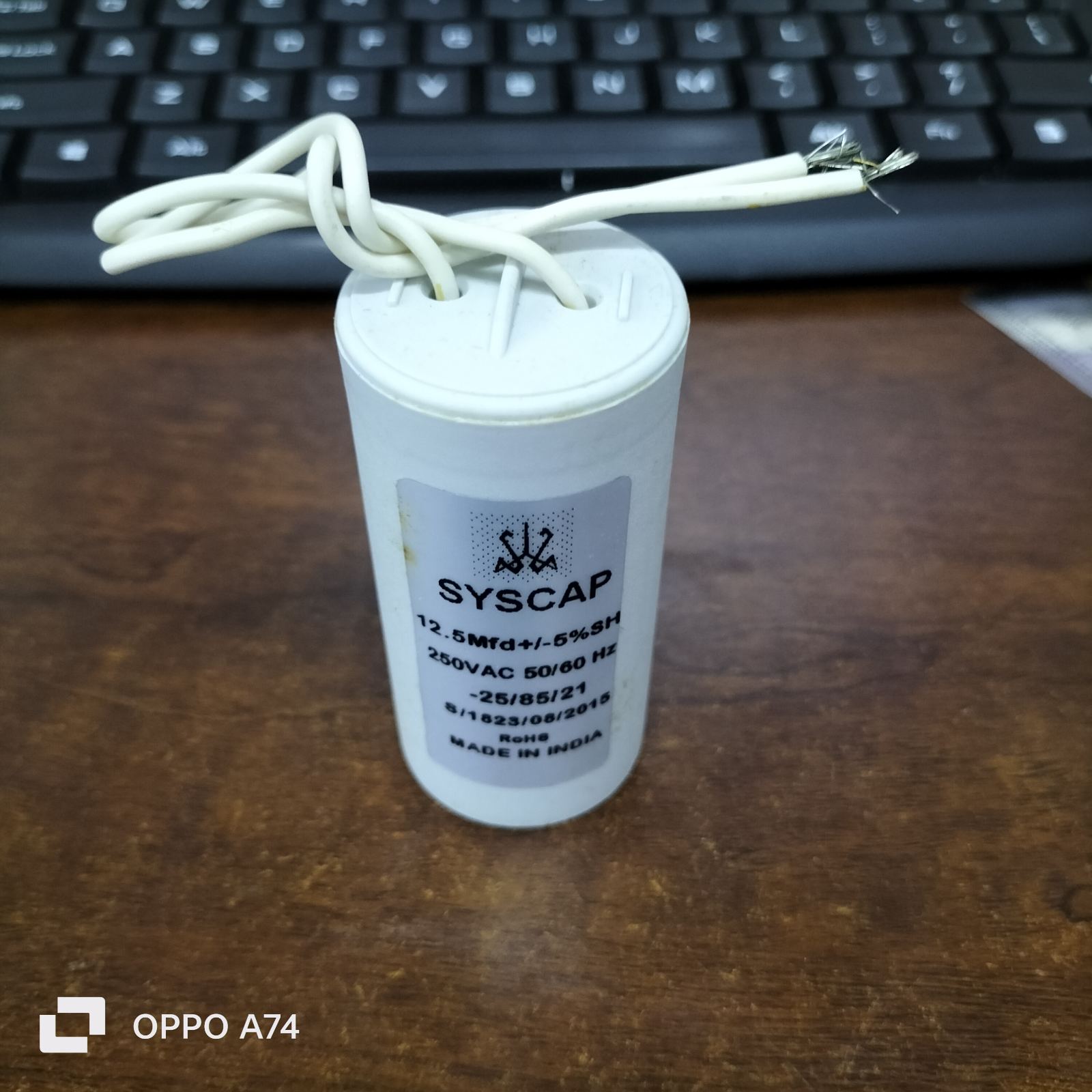 Syscap 12.5MFD 250 VAC Running Capacitor with white wires on wooden surface near keyboard