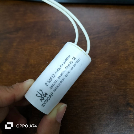 Syscap 2.0 MFD motor running capacitor white cylindrical electrical part with wires held by hand