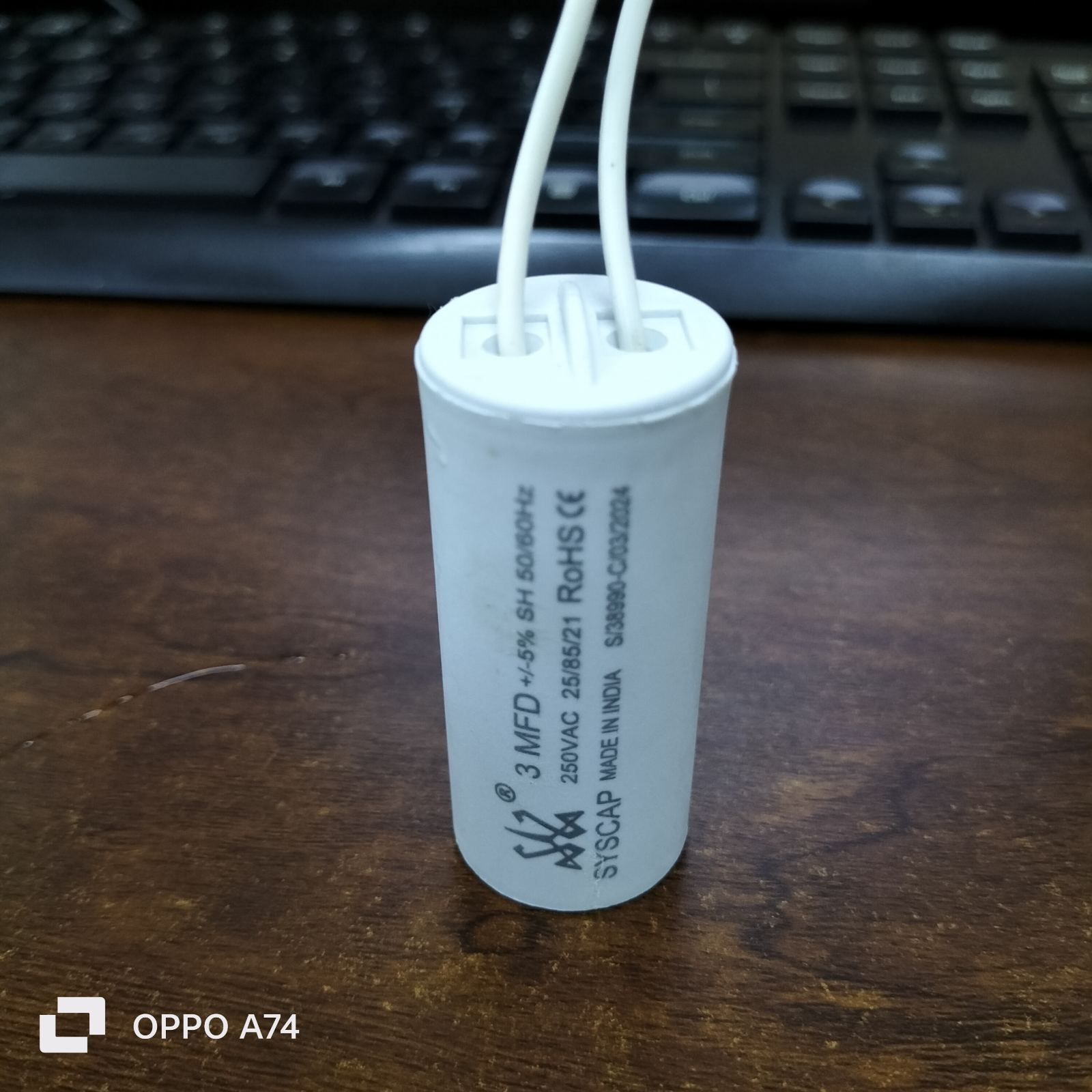 Syscap 3MFD 250 VAC Running Capacitor electrical component with white wires on wooden surface