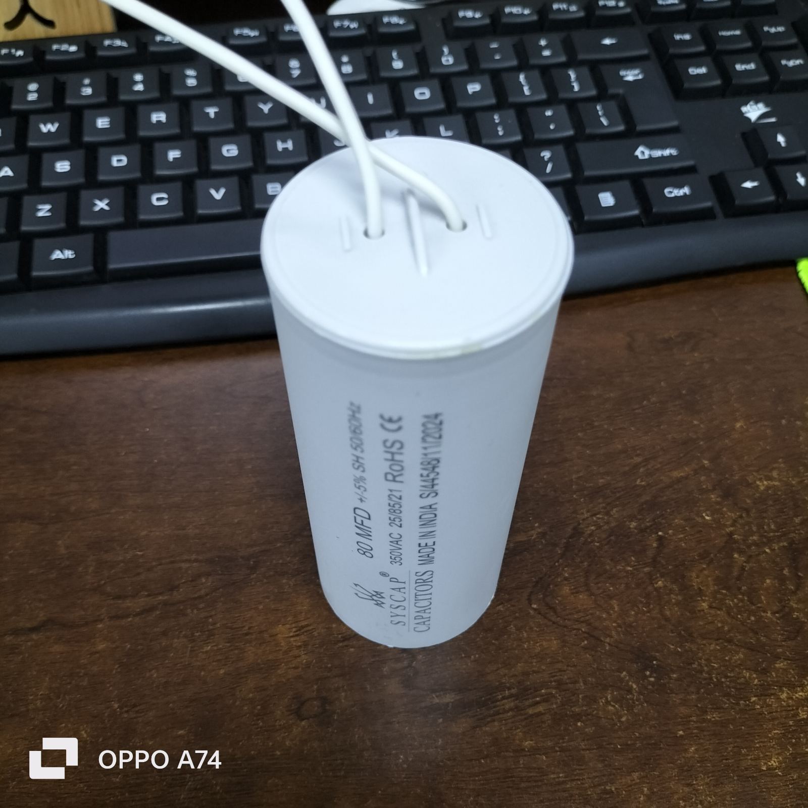 Syscap 80MFD 350V ACRunning Capacitor with white wires on a wooden desk near a black keyboard