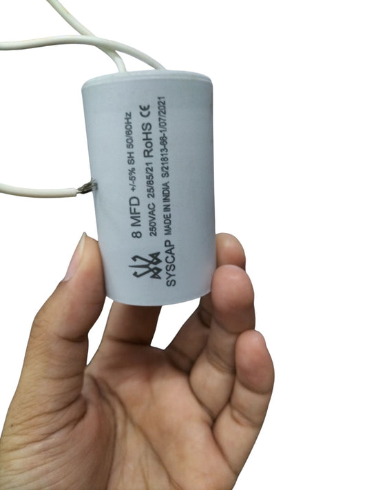 Hand holding Syscap 8MFD 250 VAC Running Capacitor electrical component with white wires