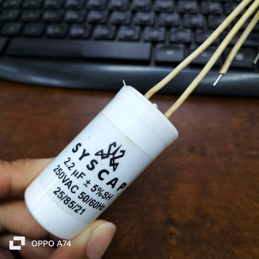 Syscap motor running capacitor 2.2mfd 250v with yellow wires held in hand over keyboard