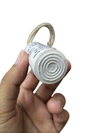 Hand holding a Syscap Motor Running Capacitor 250V AC showcasing its bottom design and wire connection