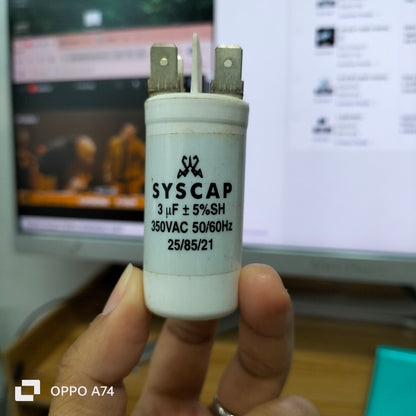 Syscap motor running capacitor 3mfd 350vac held in hand with white cylindrical body and metal terminals